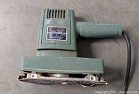 Left-side view of green Korvettes orbital sander showing sanding base and cord