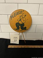 Front of round yellow metal sign showing text and cartoon figure