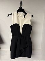 Front view of sleeveless ivory and black peplum dress on hanger