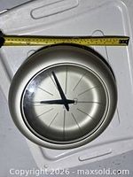 Front view of Umbra brushed metal wall clock with measuring tape showing diameter
