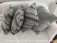 Four throw pillows on sofa: three mosaic-pattern square, one solid grey rectangular