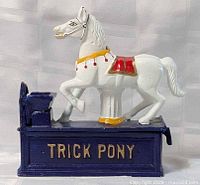 Full view of cast iron Trick Pony coin bank showing white horse on blue base