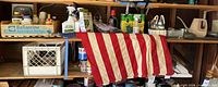 Wide view of shelf with chemicals, flag, tools, watering can, tote
