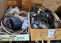 Two boxes containing assorted cords and cables, beige power strip and AC adapter visible