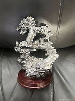 Front view of metallic silver Chinese dragon figurine on brown wood base