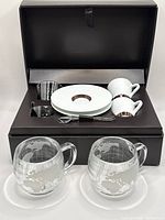 Open Nespresso presentation box showing all components with two Nestlé globe mugs in front