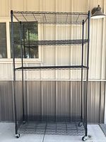 Full view of black metal wire shelving unit showing four shelves and casters