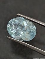 Front view of oval aquamarine held by tweezers