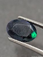 Front view of oval faceted opal in tweezers