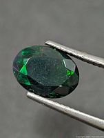 Front view of oval faceted dark opal held by tweezers
