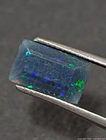 Rectangular opal held in tweezers showing blue-green flashes