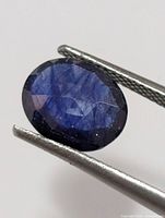Front view of oval faceted sapphire held by tweezers