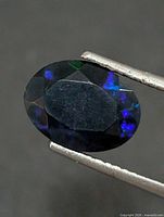Front view of oval faceted opal held in tweezers