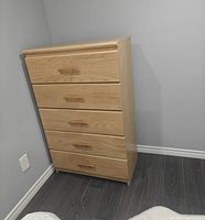 Front view of light oak 5-drawer dresser against wall