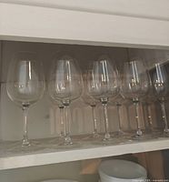 Six tall stemmed clear glass wine glasses on shelf