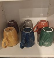 Six colored ceramic mugs upside down displaying colors and textured pattern
