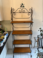 Front view of empty wrought iron baker's rack showing scrollwork and wood shelves