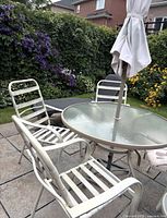 Round glass dining table, three of four chairs, umbrella visible