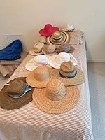 All hats laid out on bed showing variety of straw, crochet and suede styles