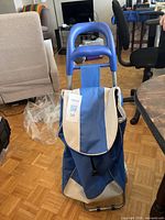 Front view of blue and beige shopping trolley showing handle, flap, bag and frame