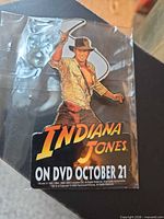 Front view of sealed Indiana Jones promotional pin badge showing artwork and release date