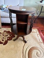 Full view of end table showing round top, open center storage, carved side panels