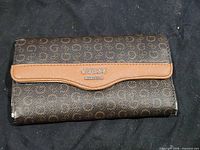 Front view of Guess wallet showing monogram print, tan trim and metal logo plaque