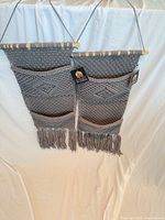 Two gray macrame wall pocket organizers hanging side by side to show full view and fringe