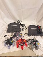 Two Nintendo 64 consoles with four controllers, cables visible