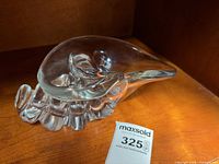 Side view of clear glass conch shell sculpture on shelf with lot tag visible