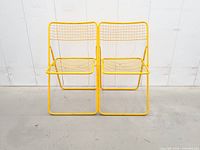 Front view of both yellow wire-mesh folding chairs standing open