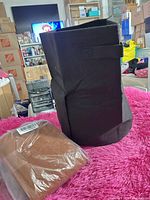 Black felt container upright beside sealed brown piece