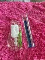 Clear plastic rain gauge with blue markings beside packaged green bracket and hardware