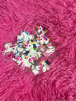 Pile of approximately 15 multicolour unicorn PVC rubber keychains on pink surface