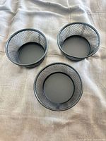 Top view of three identical black mesh desk cups