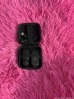 Earbuds, charging case and USB cable inside open zip case on pink surface
