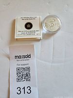 Coin in box with leaflet and lot tag visible