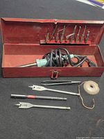 Open red metal case showing soldering iron, cord, tips in lid, drill bits, tweezers, solder spool
