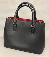 Front view of black leather satchel with red interior and gold hardware