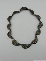 Full view of necklace laid flat showing linked paisley panels with abalone inlay