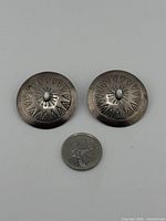 front view of the two round sterling silver earrings with stamped designs shown beside a Canadian quarter for scale