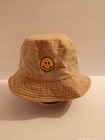 Front view of beige bucket hat showing smiley embroidery