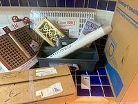 Group shot of boxed faucet, toilet seat, drawer liner, caddy, vent filters, grill mats, register grilles
