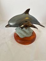 Two-dolphin bronze-tone metal sculpture on faux-stone mount and wood base front angled view