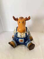 front view of ceramic moose cookie jar showing plaid shirt and blue overalls