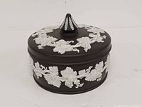 Angled view of closed trinket box showing white grapevine relief and finial