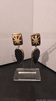 Front view of both earrings on stand showing starburst shell inlay tops and black stone leaf drops
