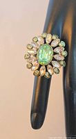 Front view of ring on display finger showing green center stone and surrounding marquise and round crystals
