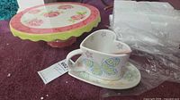 Cake stand with rose design, heart cup, saucer, spoon and packaging visible