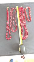 Overview of four red beaded necklaces alongside measuring tape